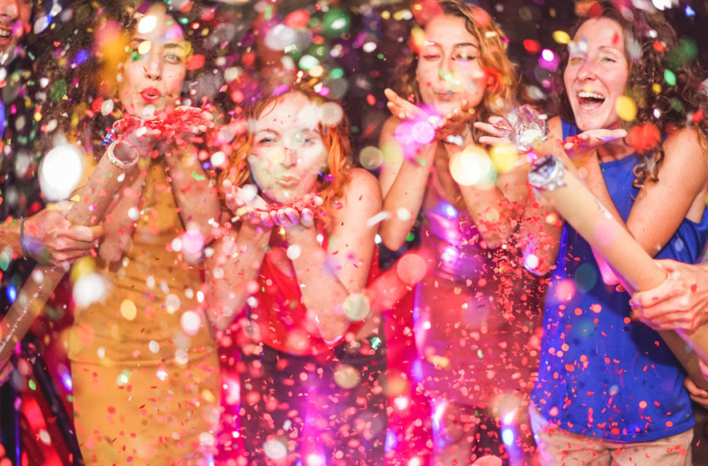 Happy friends making party throwing confetti - Young people celebrating on weekend night - Entertainment, fun, new year's eve, nightlife and fest concept - Focus on red hair girl hands